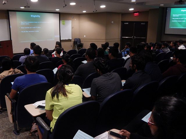This image shows a room-full of international students, backs to the camera, viewing a projector screen. The students are attending one of the ISSO's many visa and immigration-related workshops.